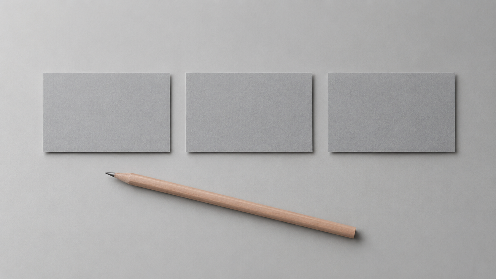 Three blank grey cards laid in a neat row on a neutral desk beside a pencil, suggesting a short plan of three shots